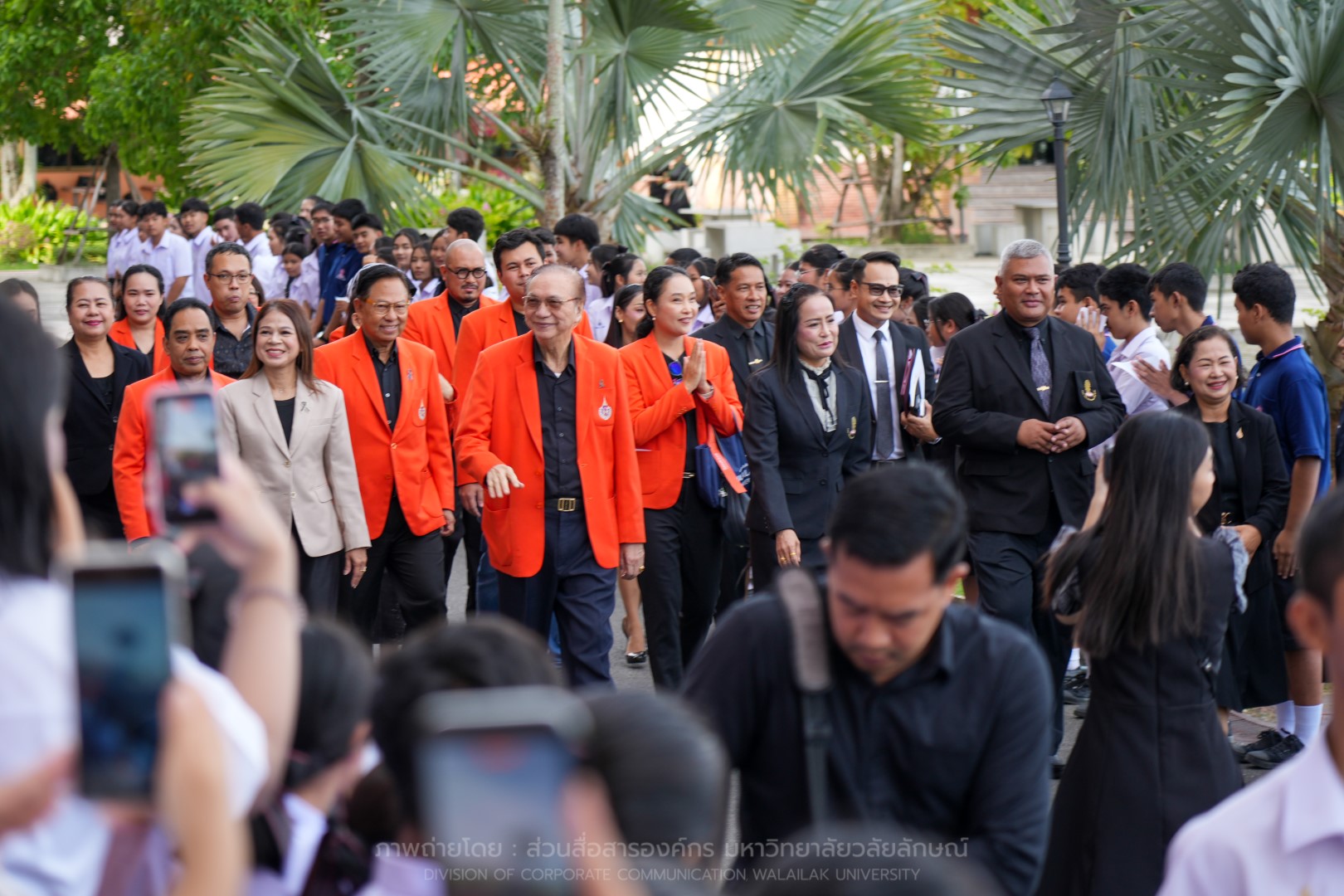Walailak University officials in orange jackets walking with students at Triam Udom Suksa School.